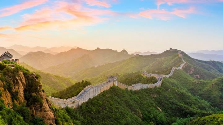 Sunset view of the Great Wall of China winding over surrounding mountains.